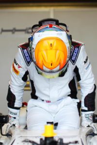 ben getting out of his car, his head is facing down showing the orange detail of his crash helmet